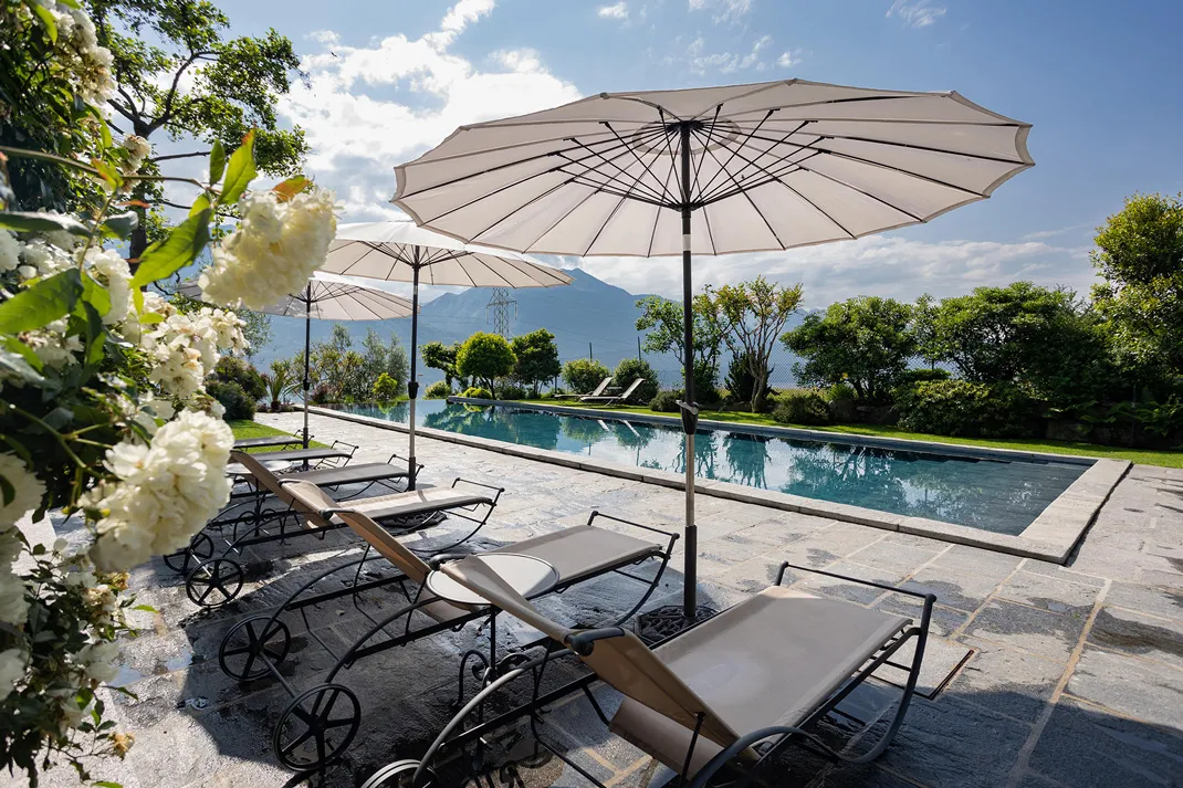 Lettini e ombrelloni a bordo piscina, con il Lago di Como e le montagne sullo sfondo