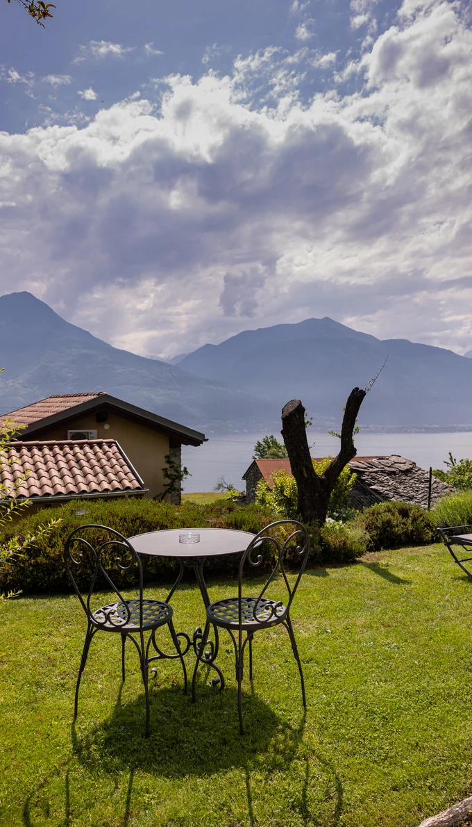 Two wrought-iron chairs and a table in the garden, with the lake and mountains beyond