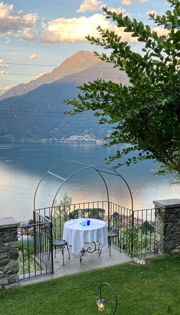 A table set for two in the garden under an iron arch, overlooking Lake Como