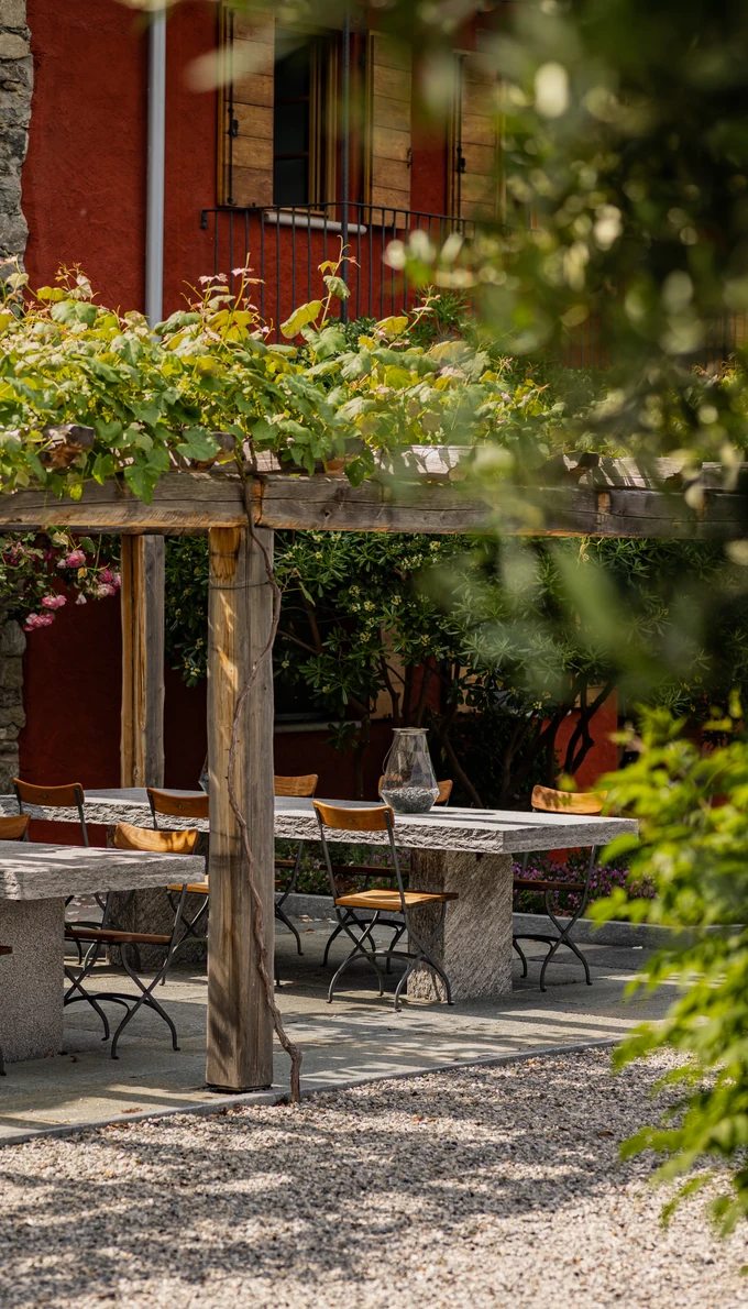 Long stone table under a wooden pergola in the courtyard of the red farmhouse